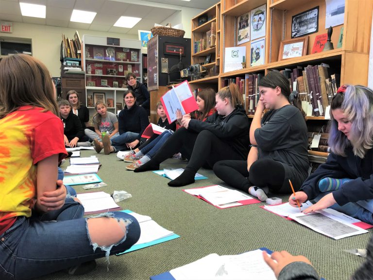 BCK students sitting in a circle with a student holding up a book.